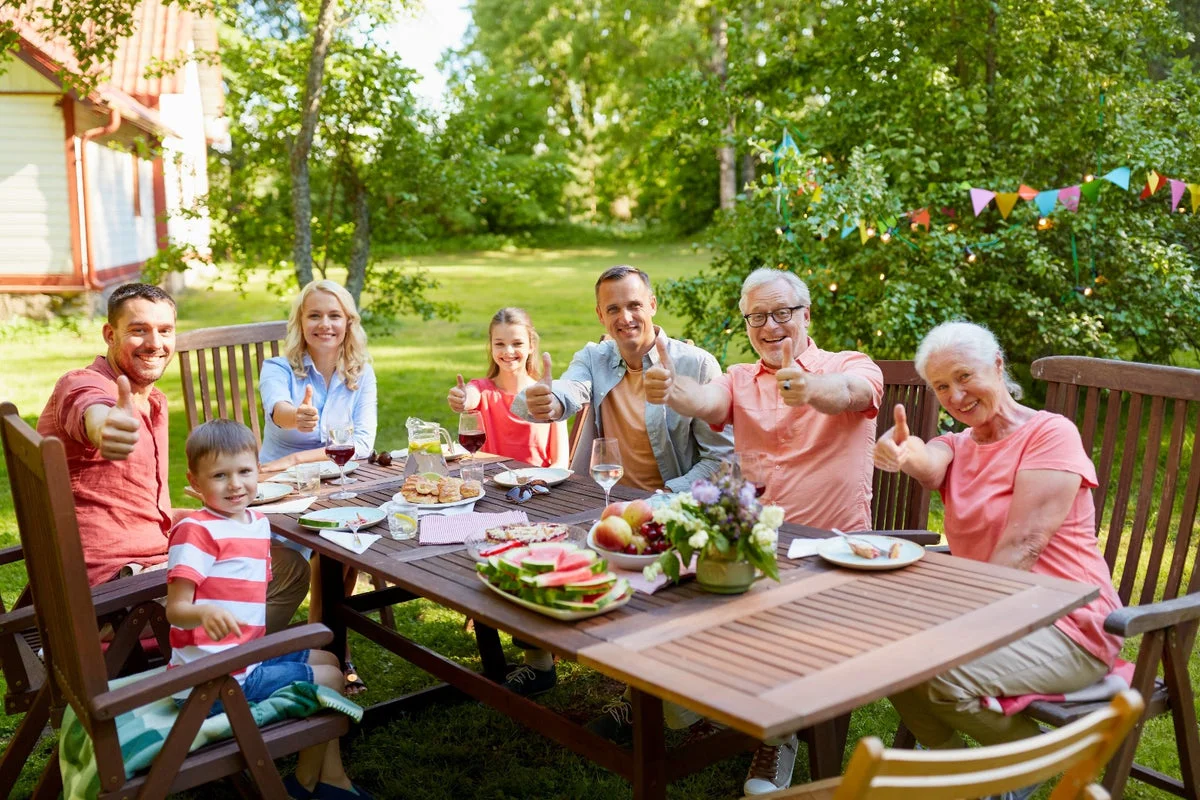 Multi-generation family giving thumbs up at an outdoor dinner table
